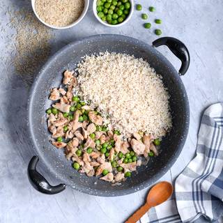 After the chickens changed their color and lost their water you can add the green peas to it as well and marinate them with salt and pepper. Finally, wash the rice and add it to the pan. 