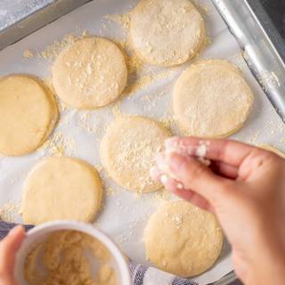 Cover a tray with parchment papers and sprinkle some corn flour on them. Place the muffins on the tray and sprinkle corn flour on them. cover the tray and let it rest for one more hour to become larger.