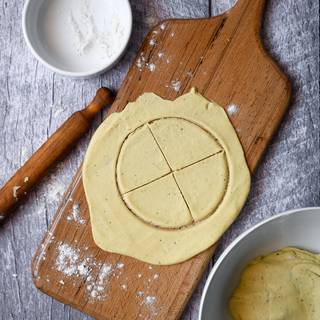 After one hour add your favorite spices to your dough and knead it until they are blended well. Sprinkle some flour on a chopping board and roll out a piece of your dough with a rolling pin. The thickness should be around 1 to 2 millimeters. Cut the dough to a circle and then cut the circle into 4 to 6 pieces.