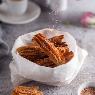 Sprinkle the cinnamon and sugar mixture on the churros immediately after removing them from the oven. The sugar won't stick to them if they are cold.