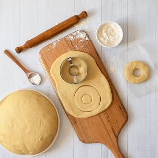 After the dough doubles in size, squeeze the dough to release the air inside it. Sprinkle some flour on an even surface and flatten the dough on top of it with a rolling pin. Cut the dough with a doughnut cutter and place them on the parchment paper.